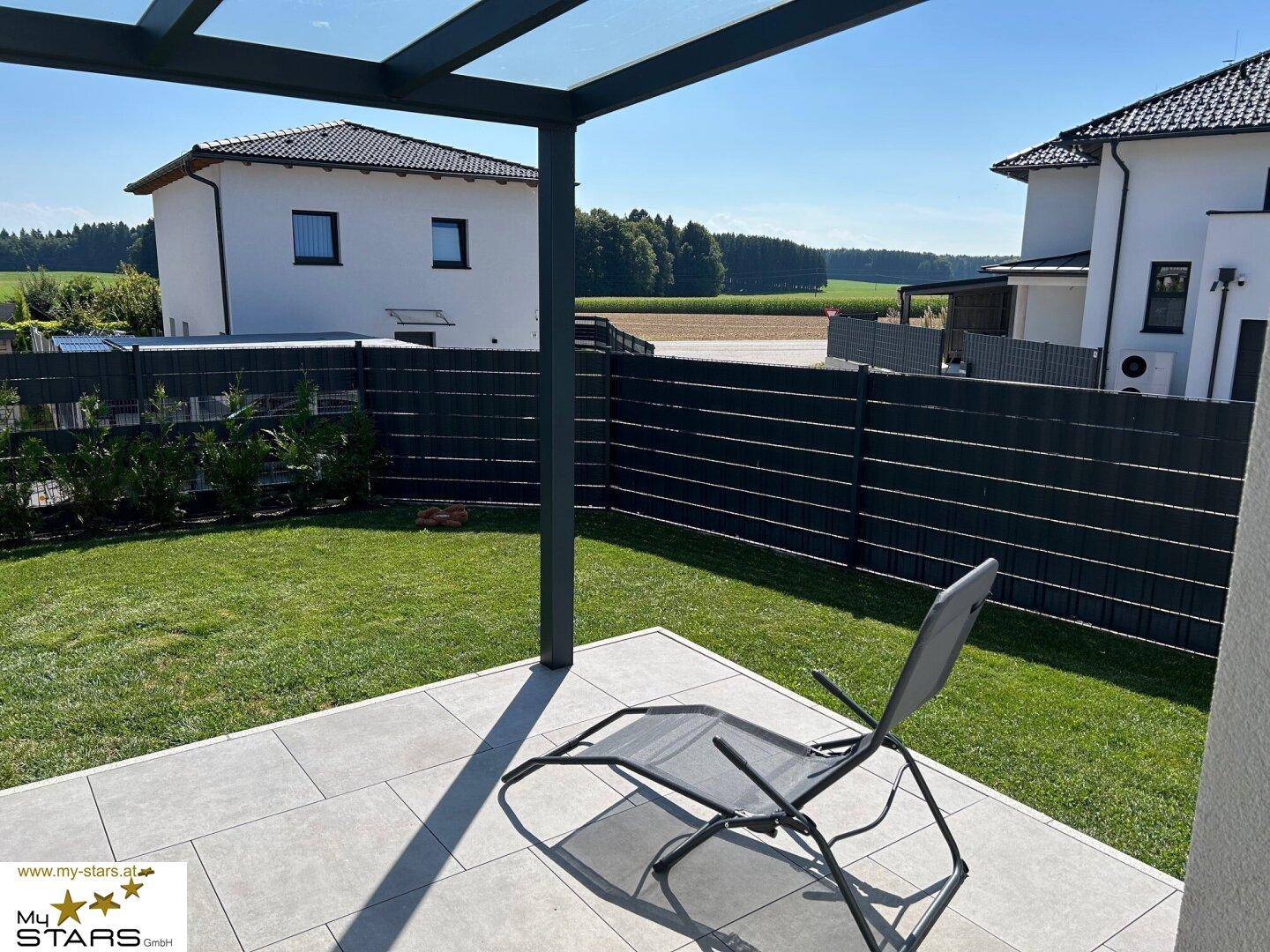 Entspannungsbereich auf der überdachten Terrasse mit Blick auf den grünen Garten und weite Felder.