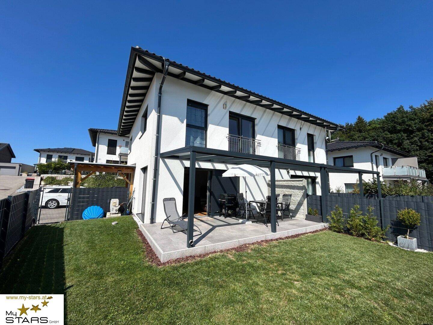 Moderne Hausfassade mit überdachter Terrasse, Gartenmöbeln und gepflegtem Rasenbereich.