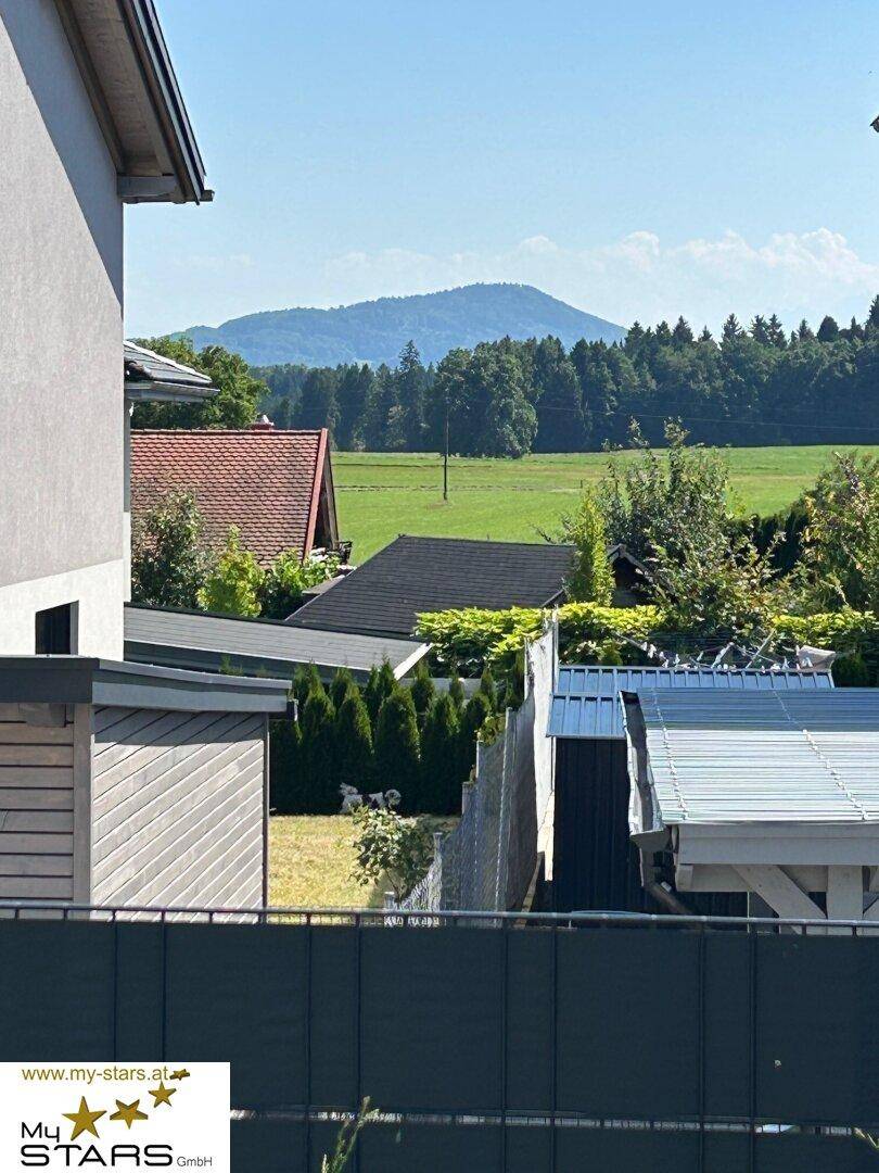 Malerischer Ausblick auf die umliegende Landschaft mit Häusern, Feldern und Bergen am Horizont.