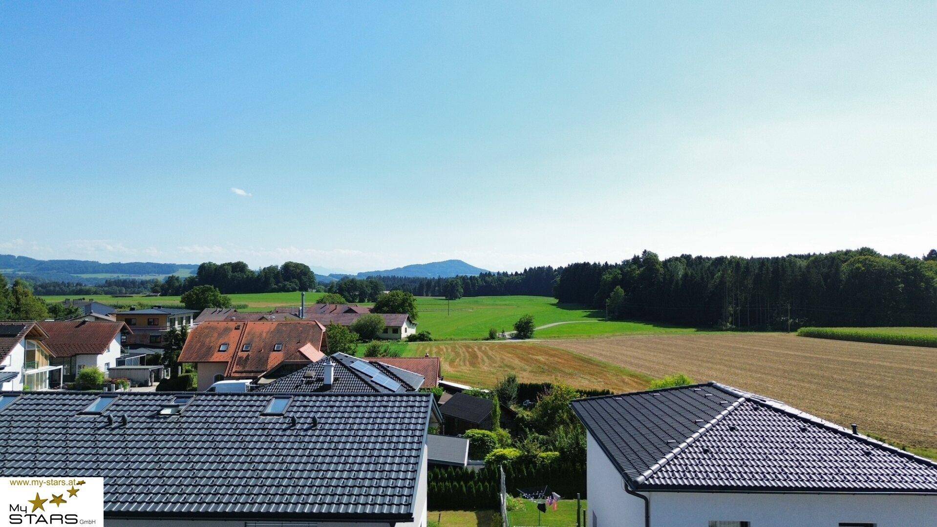 Weitläufiger Panoramablick über Dächer, grüne Felder und die sanfte Hügellandschaft in der Ferne.