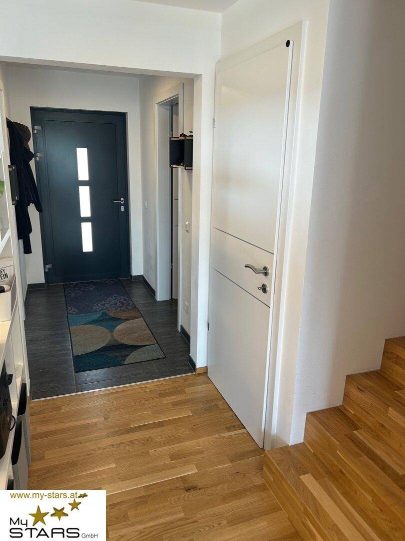 Heller Eingangsbereich mit dunkler Haustür, Holzboden und Treppe zum Obergeschoss.