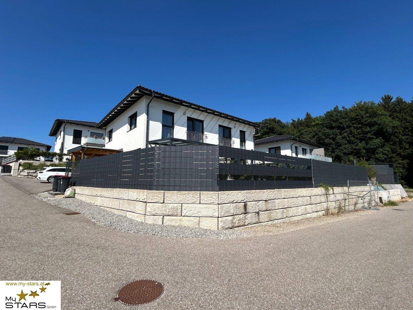 Ansicht des modernen Hauses von der Straße mit Steinfassade und gepflegtem Vorgartenbereich.