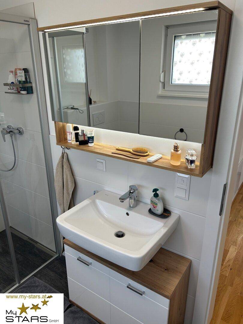 Waschbecken mit Unterschrank und beleuchtetem Spiegelschrank in einem modernen Badezimmer.
