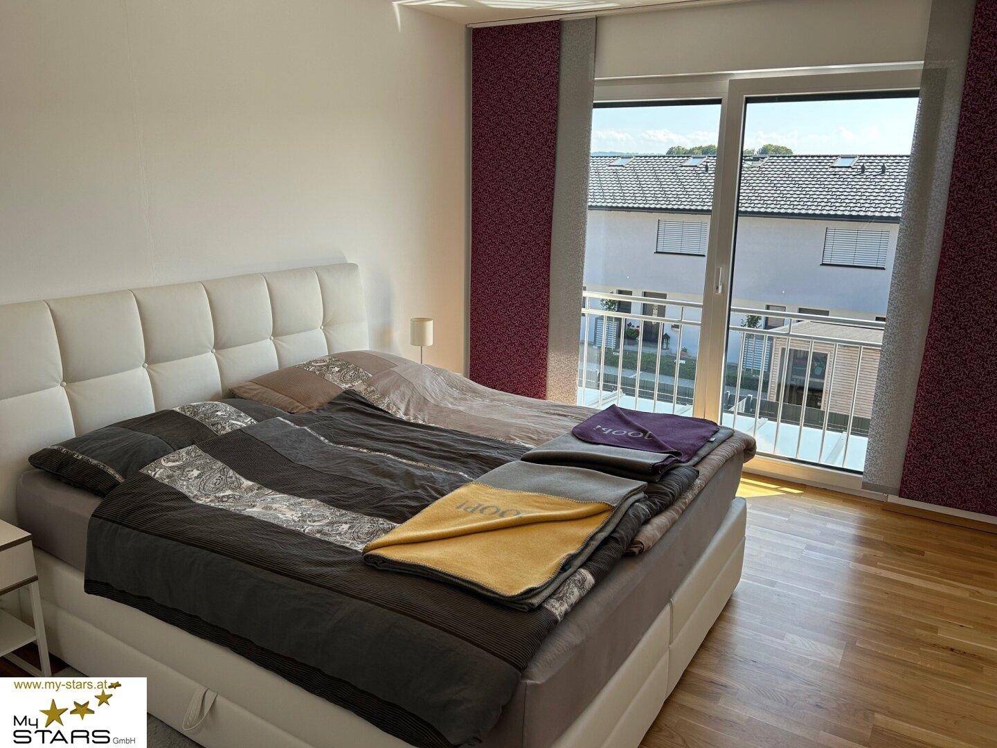 Gemütliches Schlafzimmer mit großem Bett, Holzboden und direktem Zugang zum Balkon.