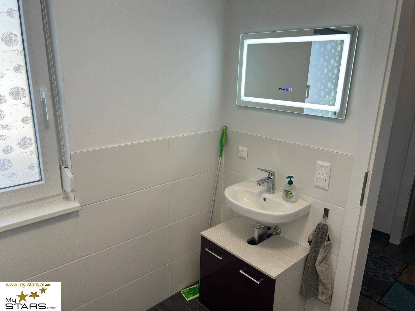 Modernes Gäste-WC mit kleinem Waschbecken, Unterschrank und beleuchtetem Spiegel.