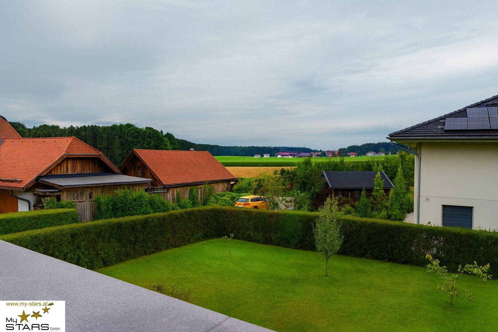 Blick von der Terrasse auf den gepflegten Garten, Nachbarhäuser und die ländliche Umgebung.