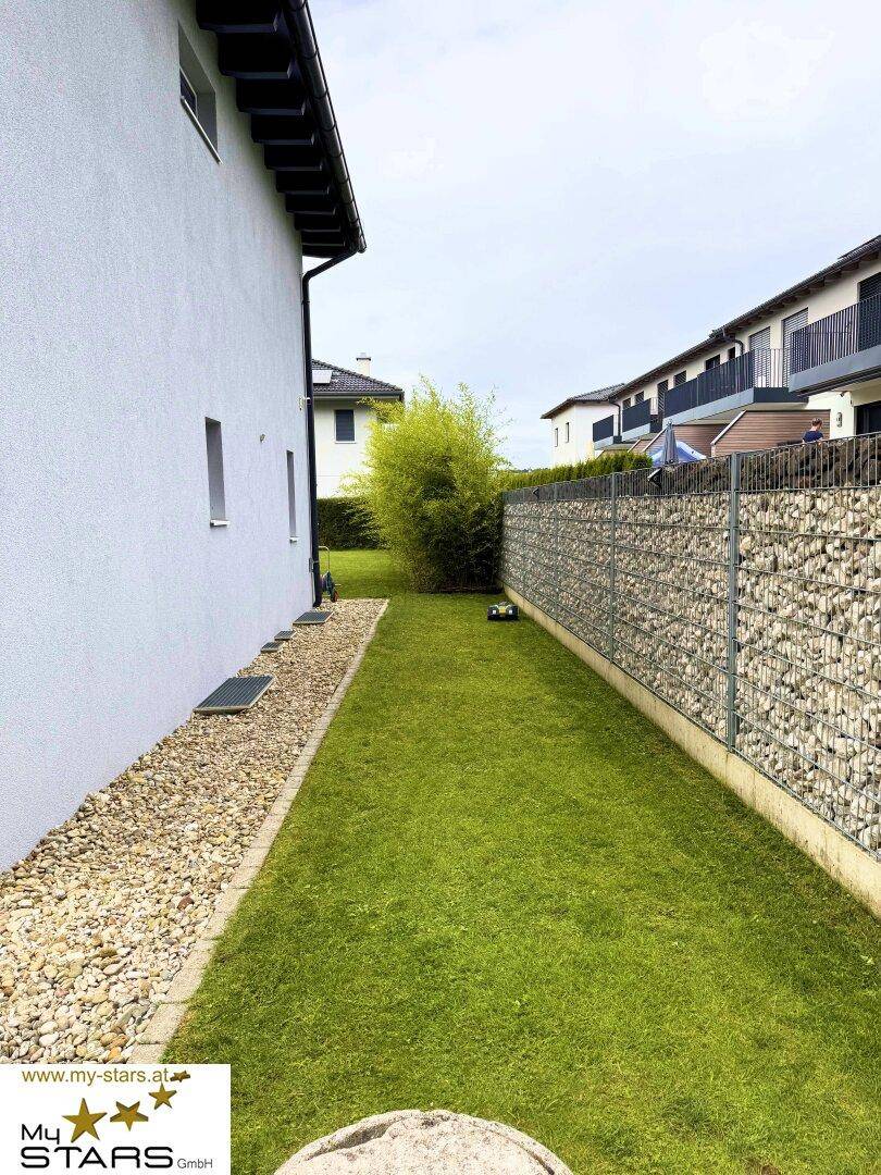 Seitenansicht des Hauses mit schmalem Rasenstreifen und einer Gabionenwand.