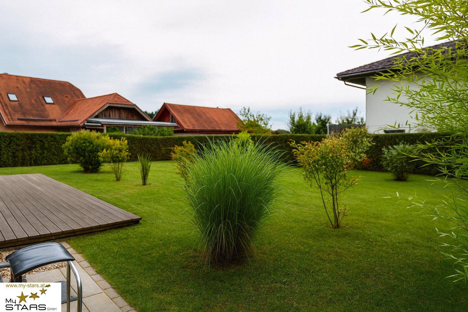 Gepflegter Gartenbereich mit Rasenfläche, Ziersträuchern und einer Holzterrasse.