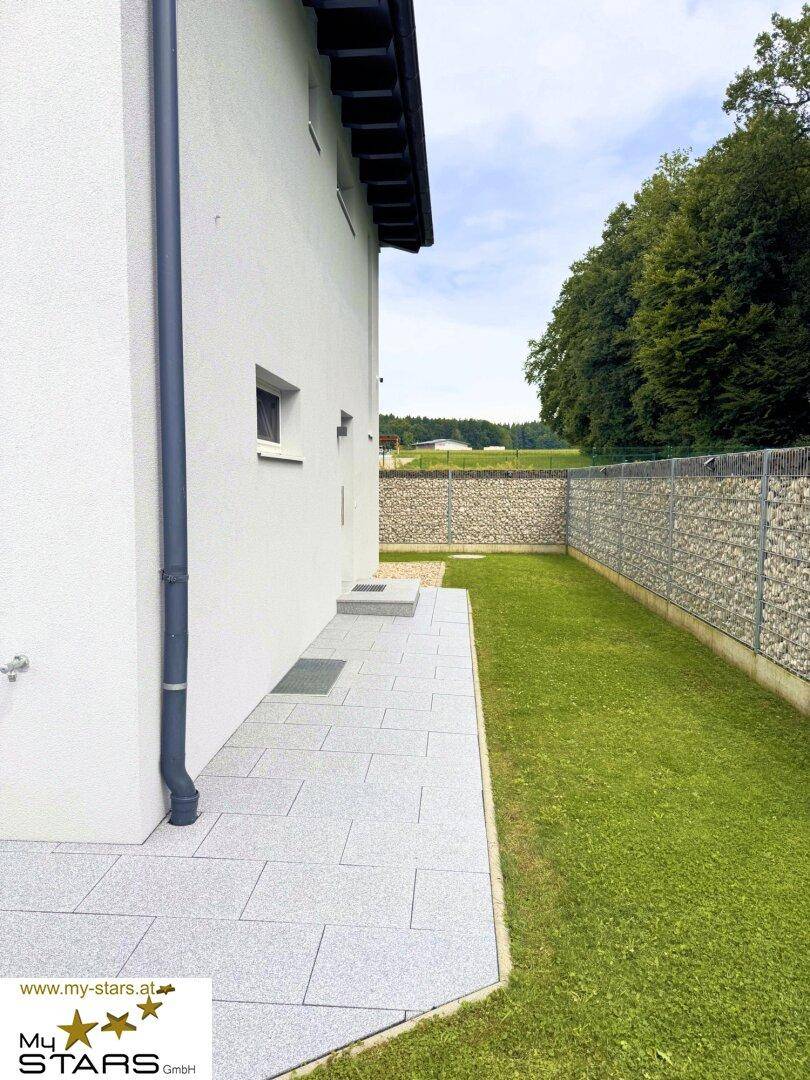 Seitlicher Zugang zum Haus mit gepflastertem Weg und angrenzendem Rasenbereich.