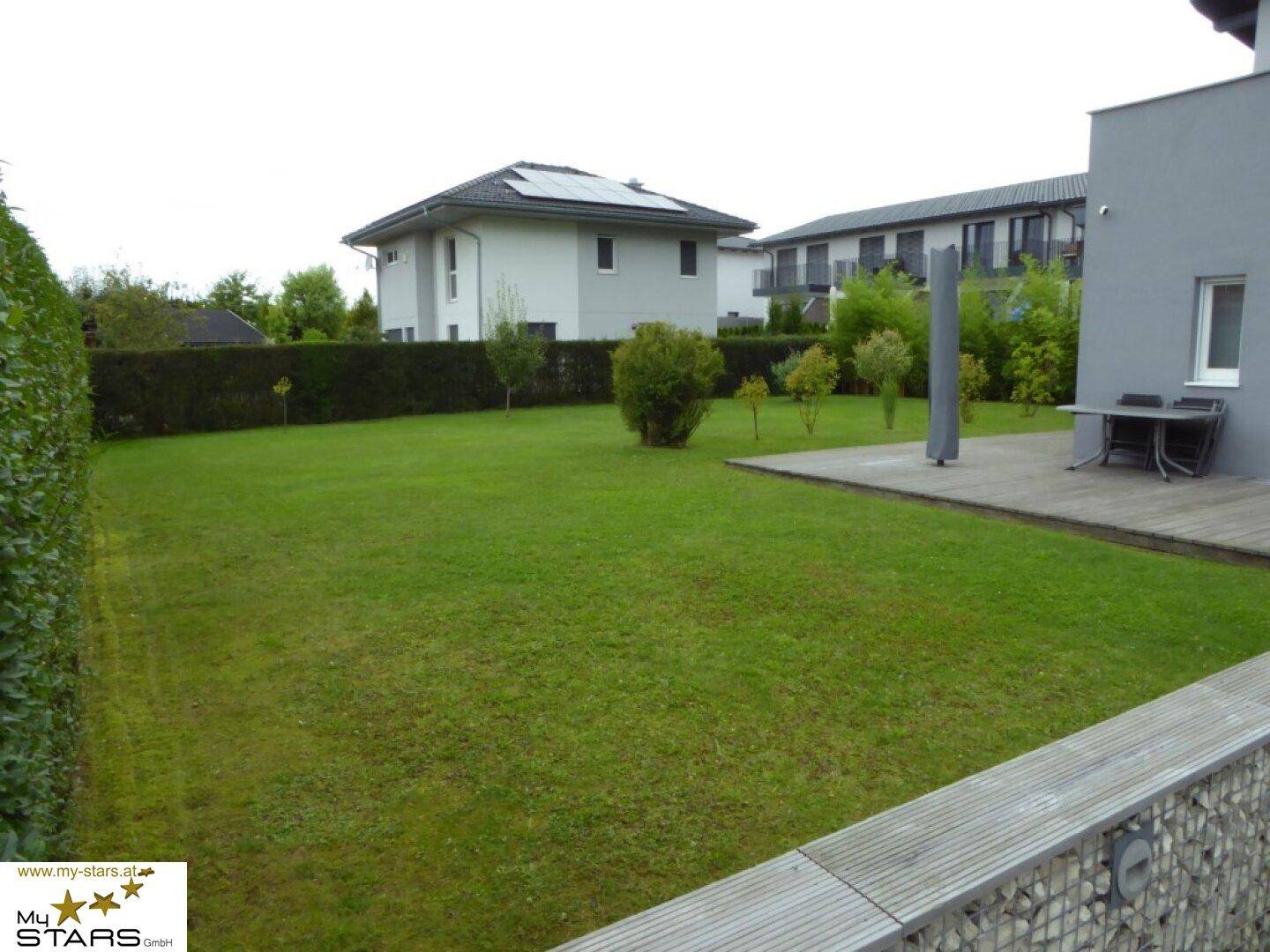 Weitläufiger, gepflegter Garten mit Rasenfläche, Hecke und angrenzender Terrasse.