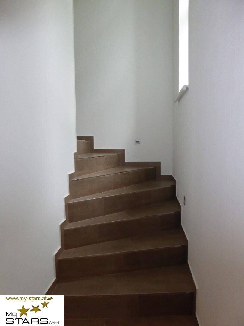 Elegante Holztreppe mit schlichten weißen Wänden, die die Stockwerke verbindet.