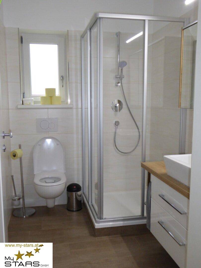 Modernes Badezimmer mit Duschkabine, Toilette, Waschbecken und Fenster.