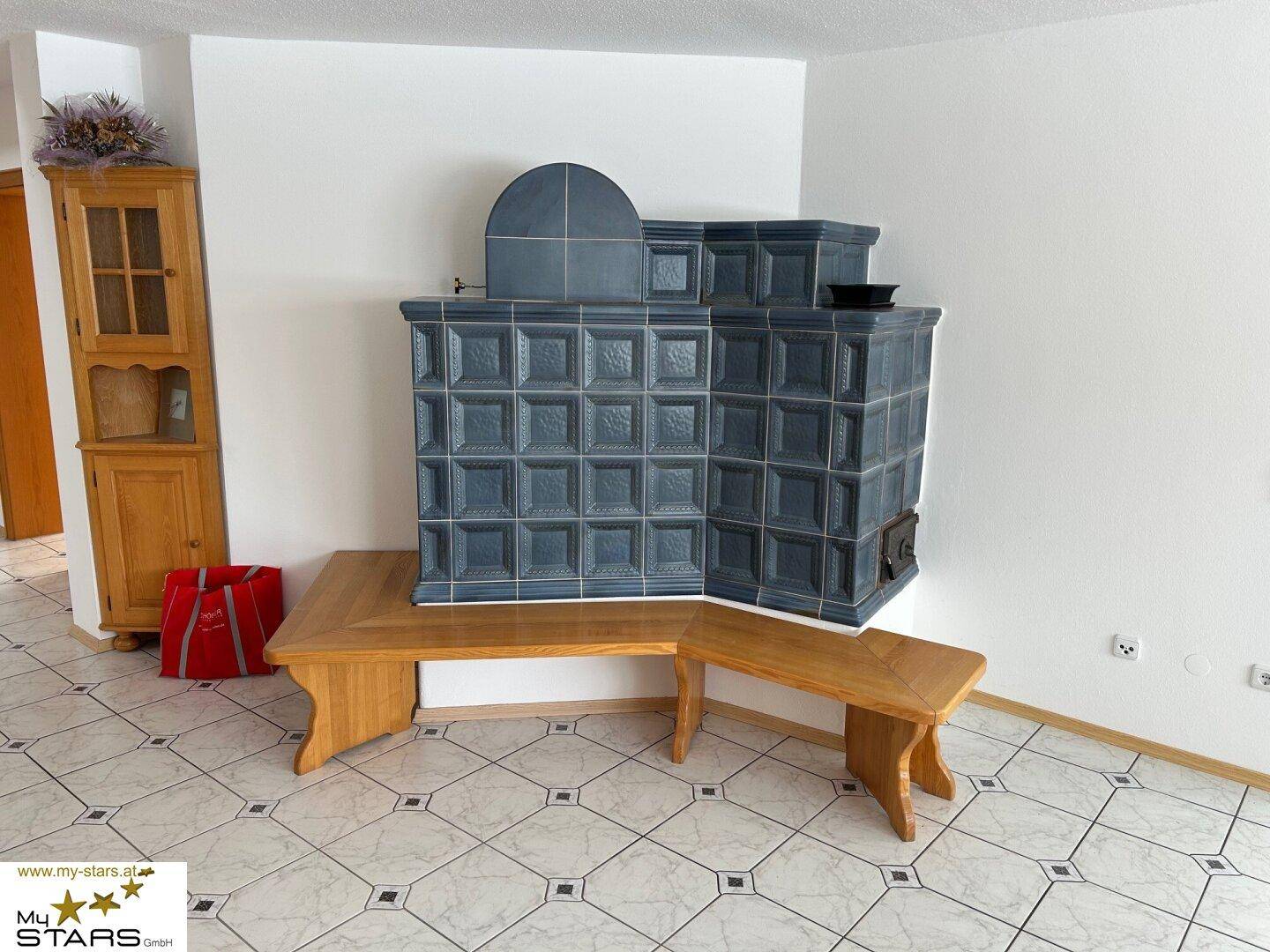 Wohnbereich mit traditionellem Kachelofen und Fliesenboden, ergänzt durch Holzmöbel.