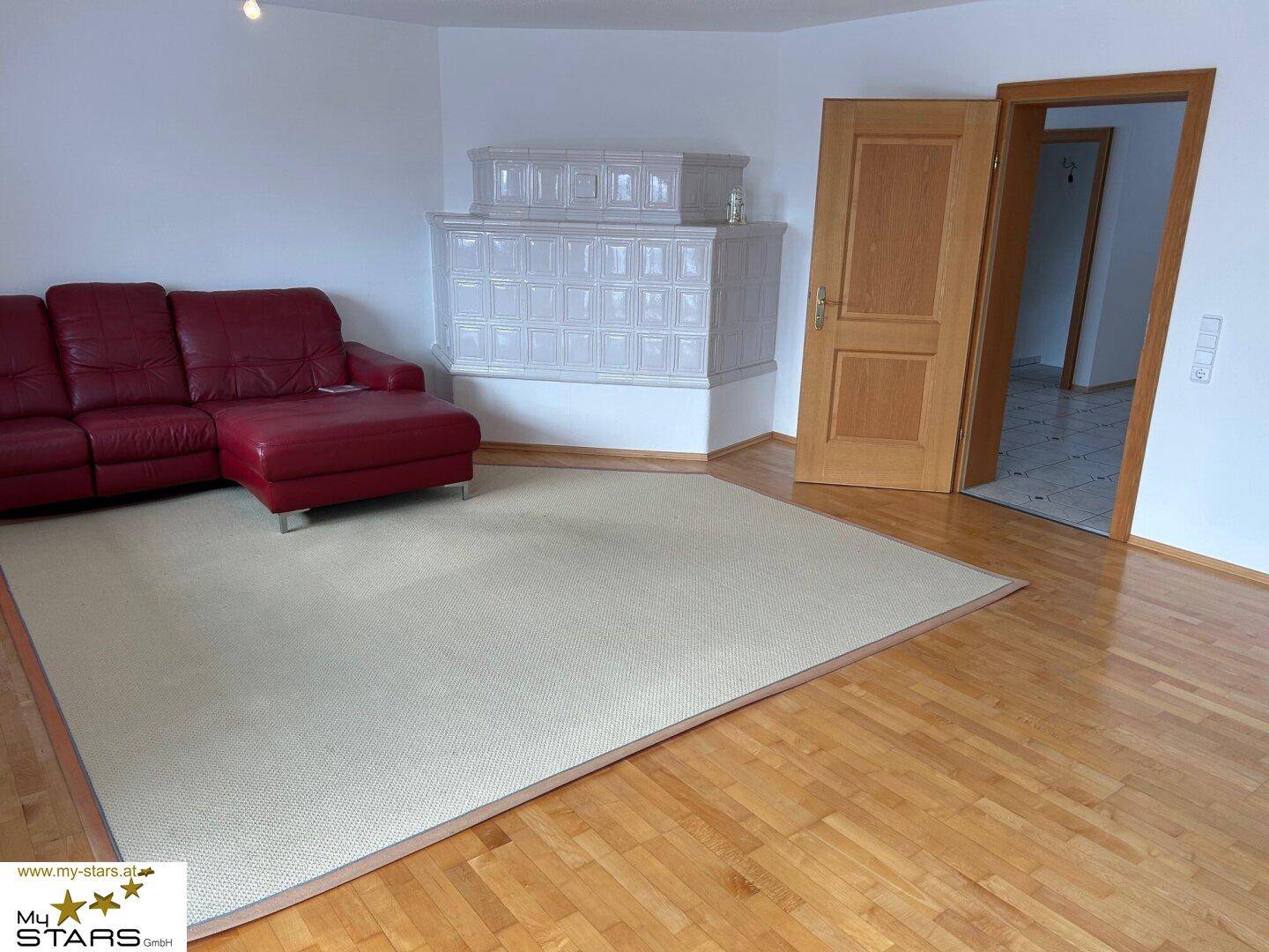 Gemütliches Wohnzimmer mit Parkettboden, rotem Sofa und weißem Kachelofen.
