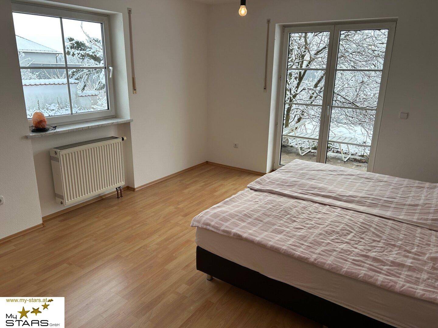Schlafzimmer mit Laminatboden, Doppelbett und Zugang zu einem Außenbereich.