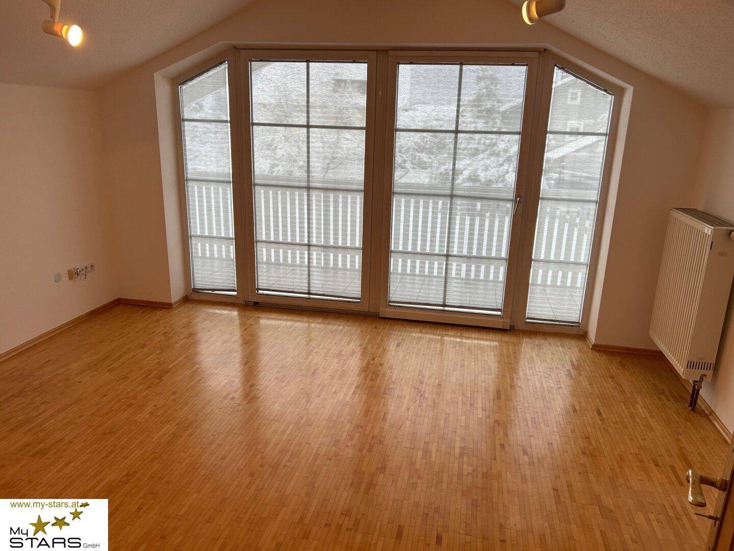 Helles Zimmer mit Parkettboden und großem Fenster mit Zugang zum Balkon.