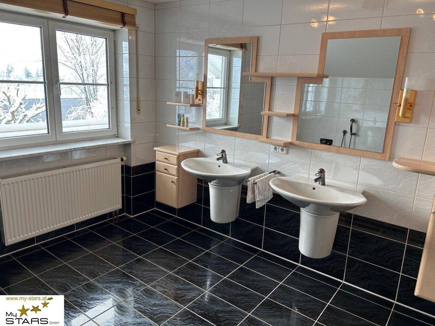 Helles Badezimmer mit Doppelwaschbecken, Fliesen und Fenster unter Dachschräge.