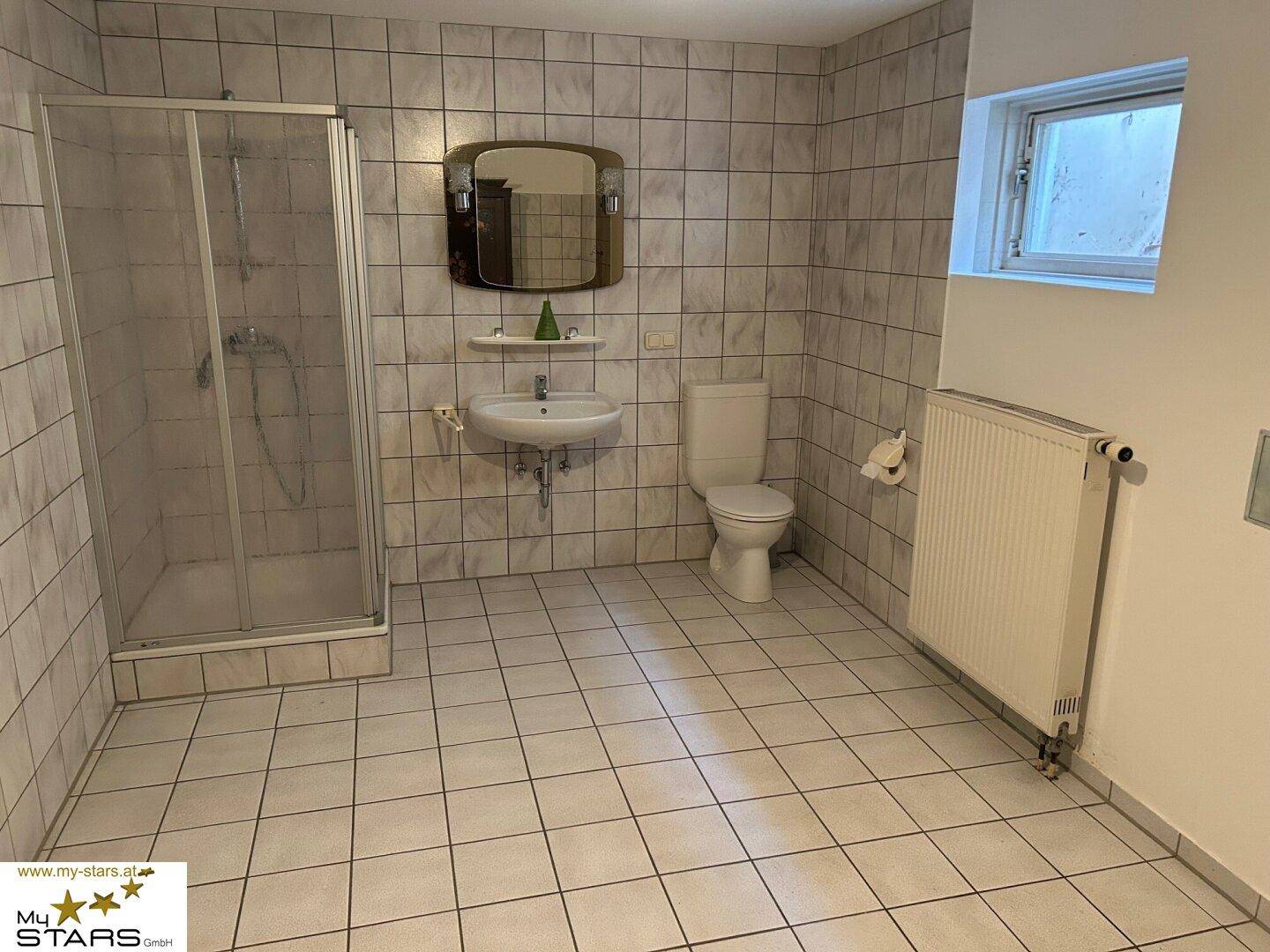 Geräumiges Badezimmer mit Dusche, WC, Waschbecken und Fenster.