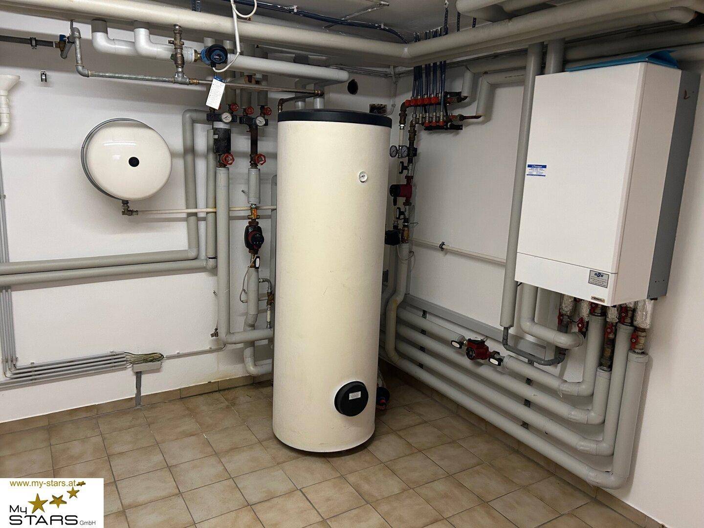 Heizungsraum mit Warmwasserspeicher und umfangreicher Rohrinstallation.