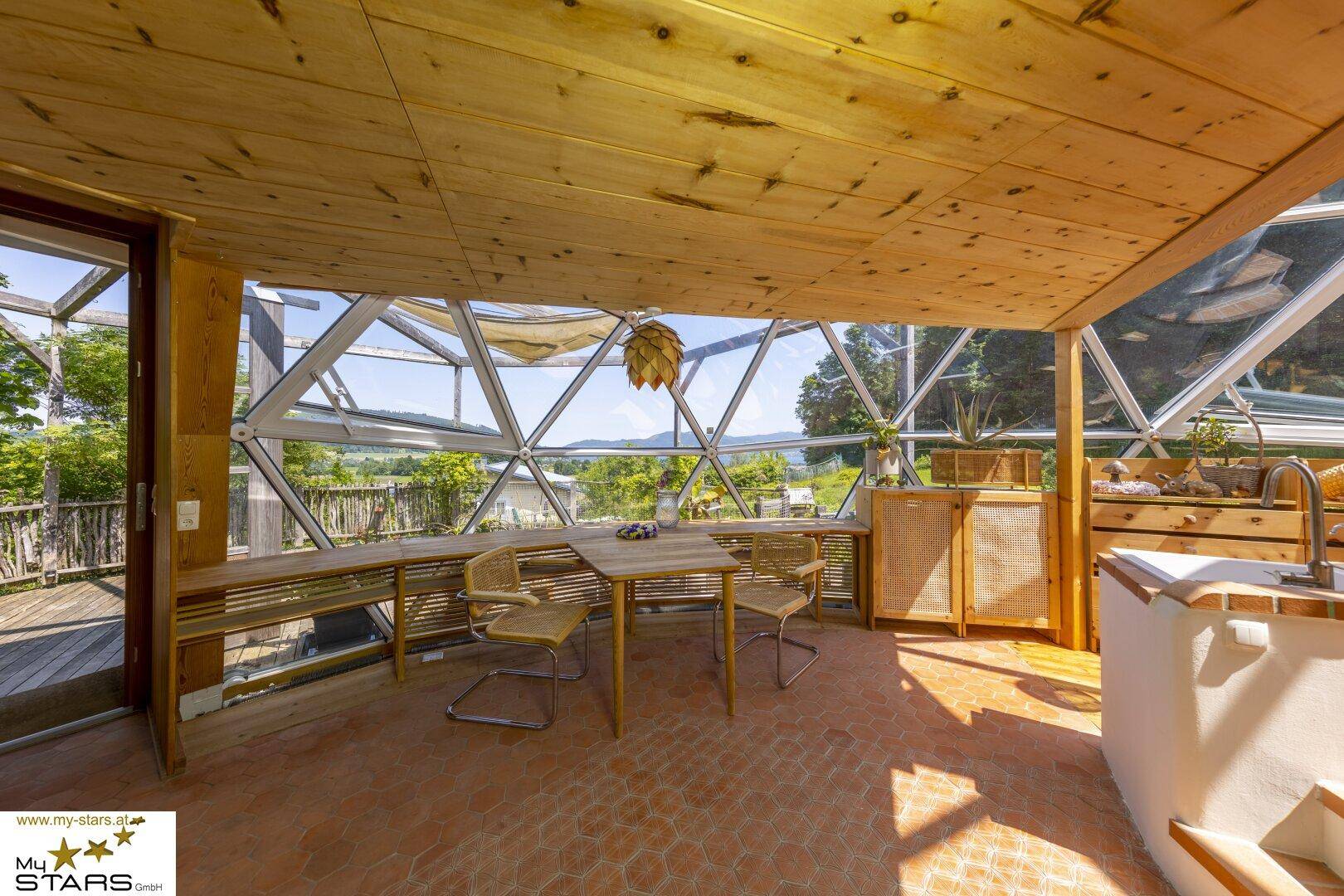 Heller Essbereich in einem Wintergarten mit Holzdach und Panoramablick auf die Landschaft.