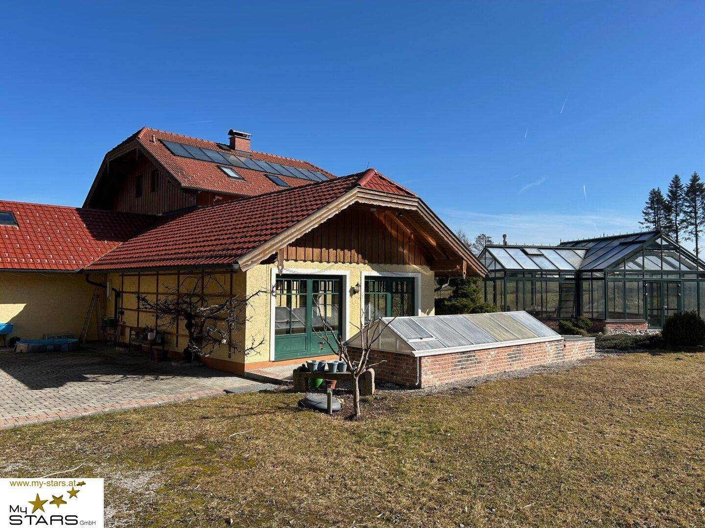 Haupthaus mit traditioneller Architektur und einem kleinen Gewächshaus im Vorgartenbereich.