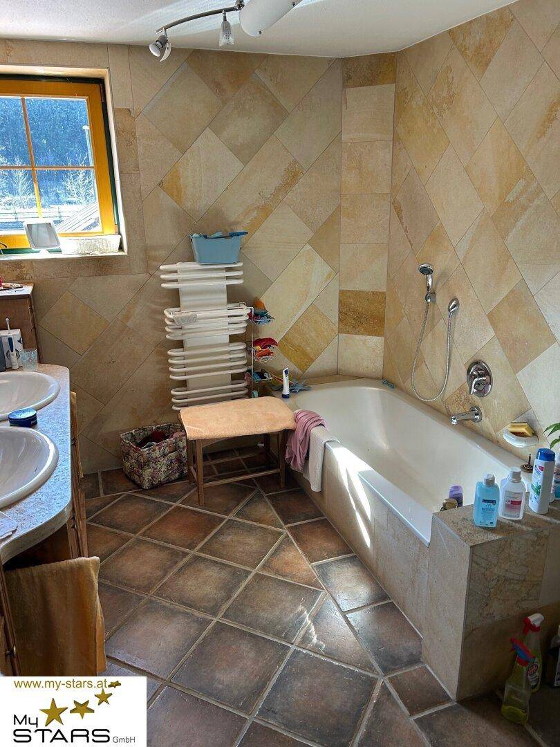 Geräumiges Badezimmer mit Badewanne, doppelter Waschtisch und Natursteinfliesen, hell und einladend.