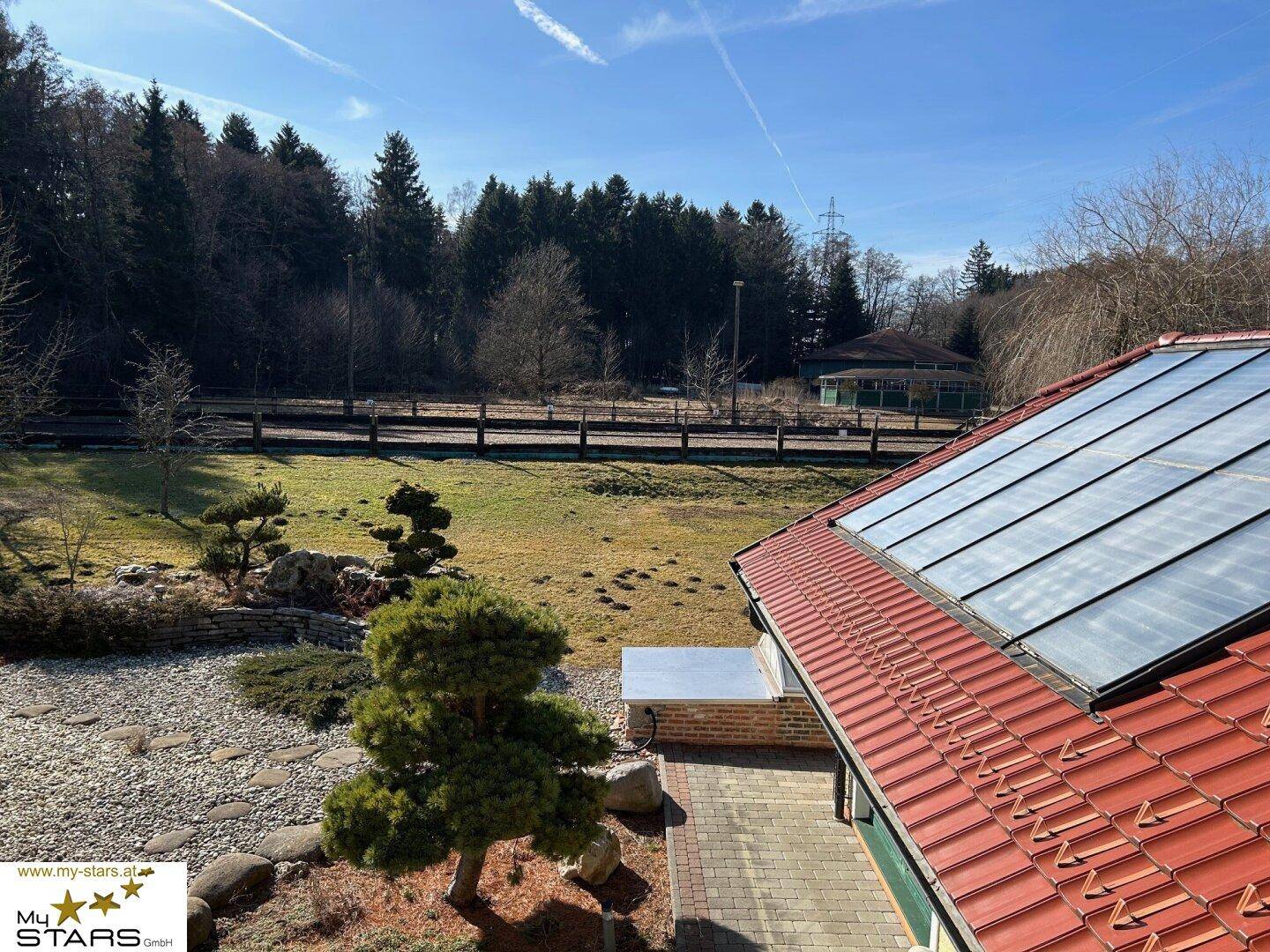 Dachansicht mit Solarpaneelen und weitem Blick über die grüne Landschaft und Wälder.