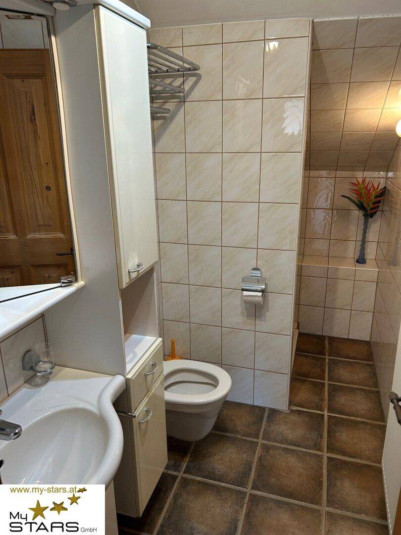 Kleines Badezimmer mit Dusche, WC und Waschbecken, komplett gefliest in hellen Farbtönen.