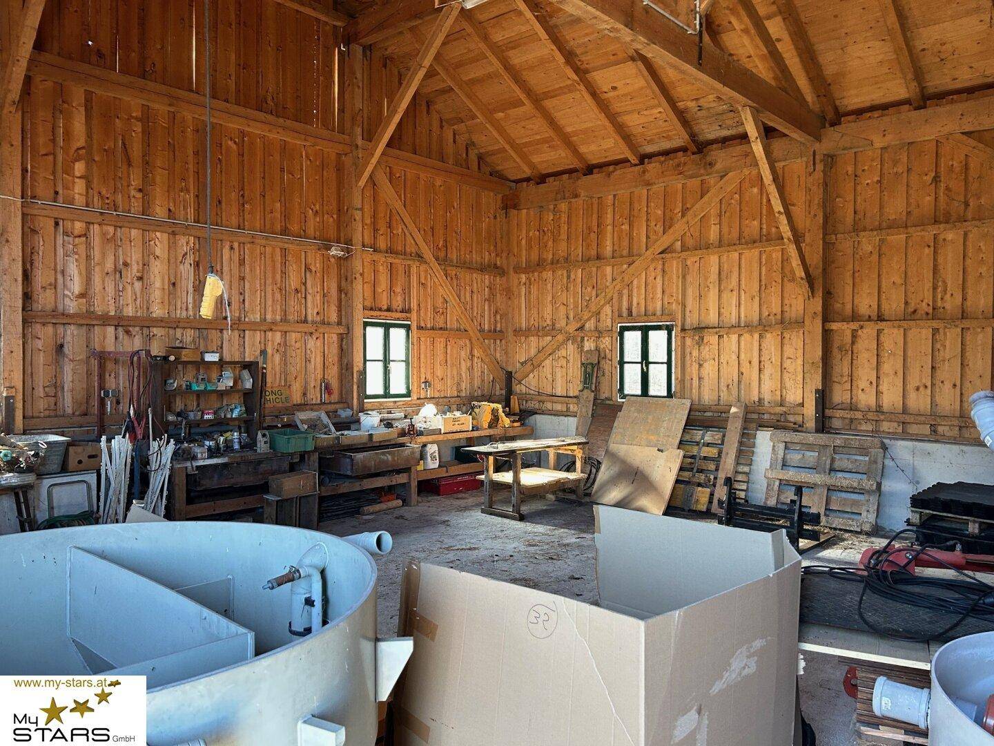 Großer Holzraum mit Werkbänken und Fenstern, ideal als Werkstatt oder Lagerfläche.