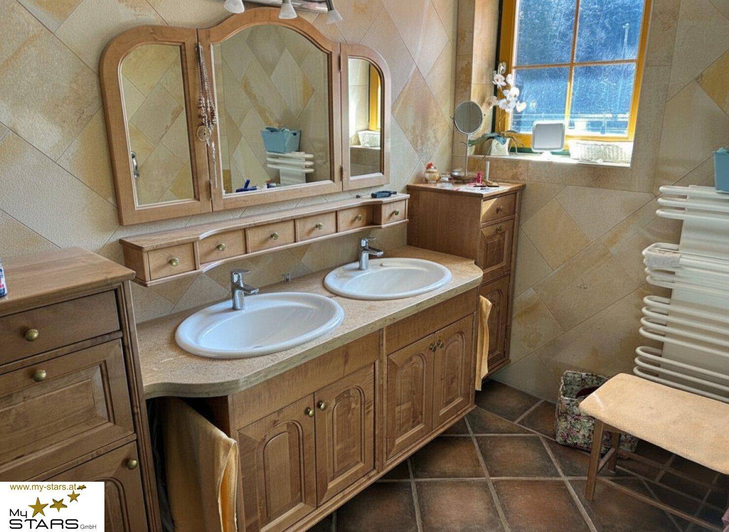 Badezimmer mit zwei Waschbecken, großem Spiegelschrank und Natursteinfliesen, bietet viel Platz.
