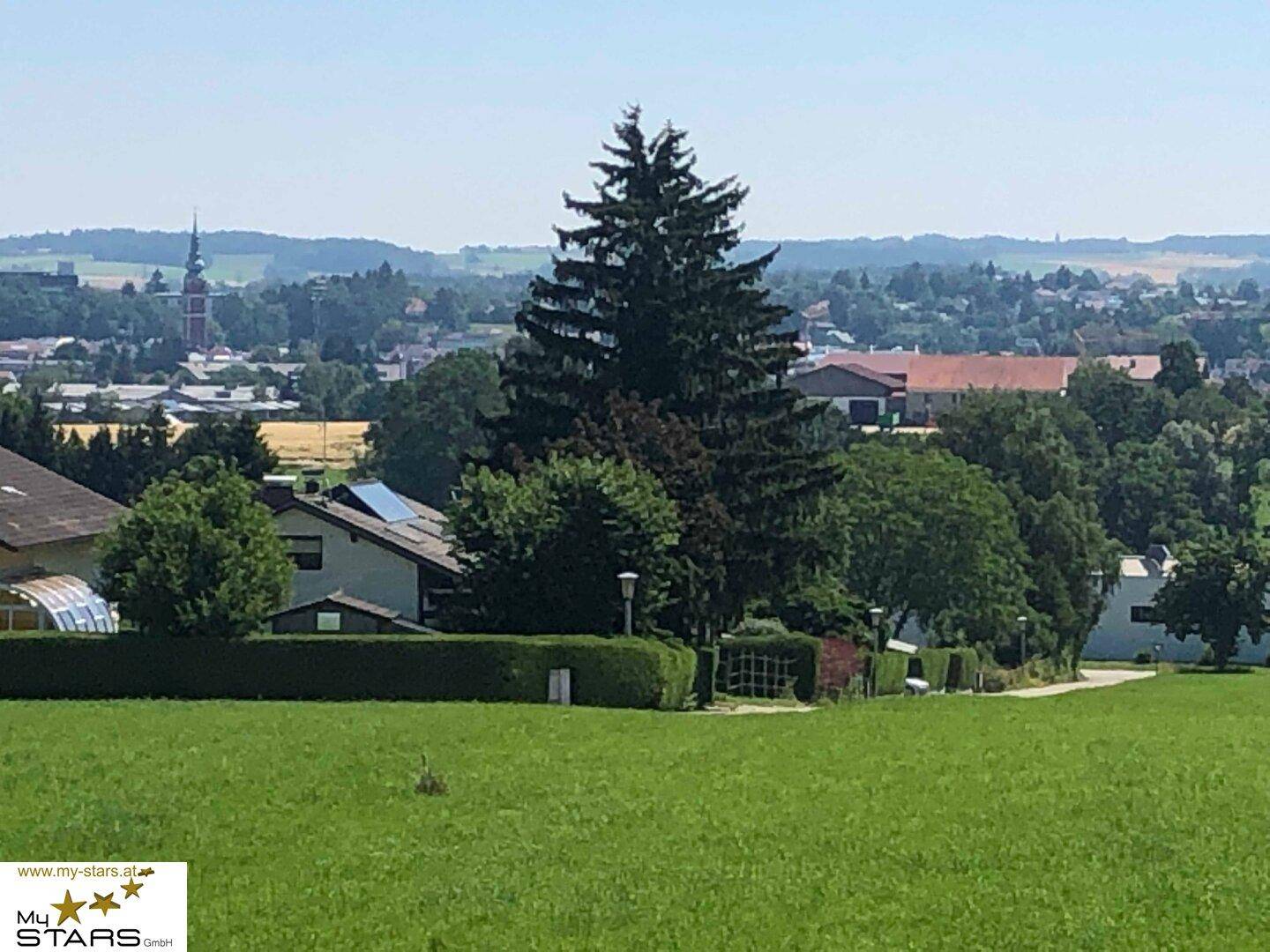 Weitläufiger Blick über die grüne Landschaft mit Häusern und einem Kirchturm in der Ferne.