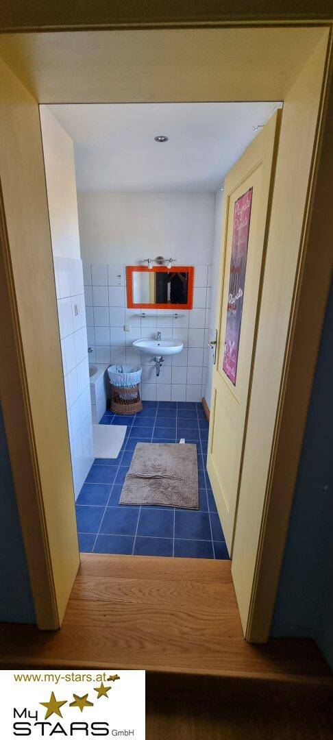 Kleines Badezimmer mit blauen Fliesen, weißem Waschbecken und orangefarbenem Spiegel.
