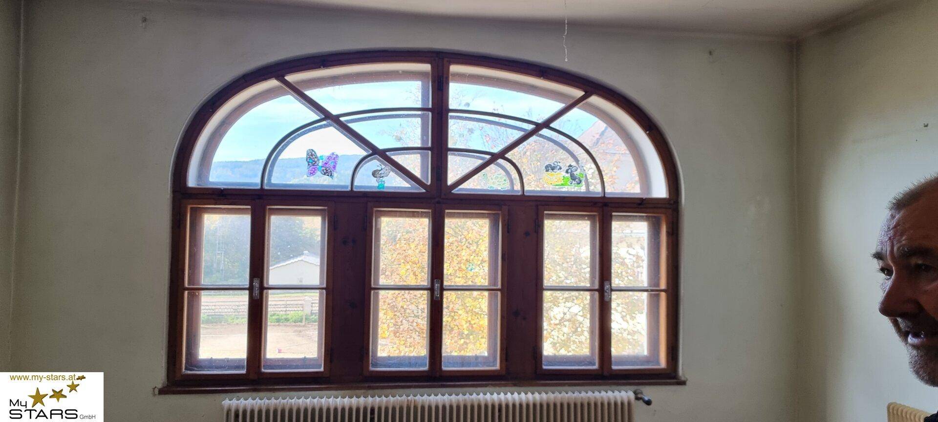 Großes, bogenförmiges Fenster mit Holzrahmen und Blick auf die Landschaft.