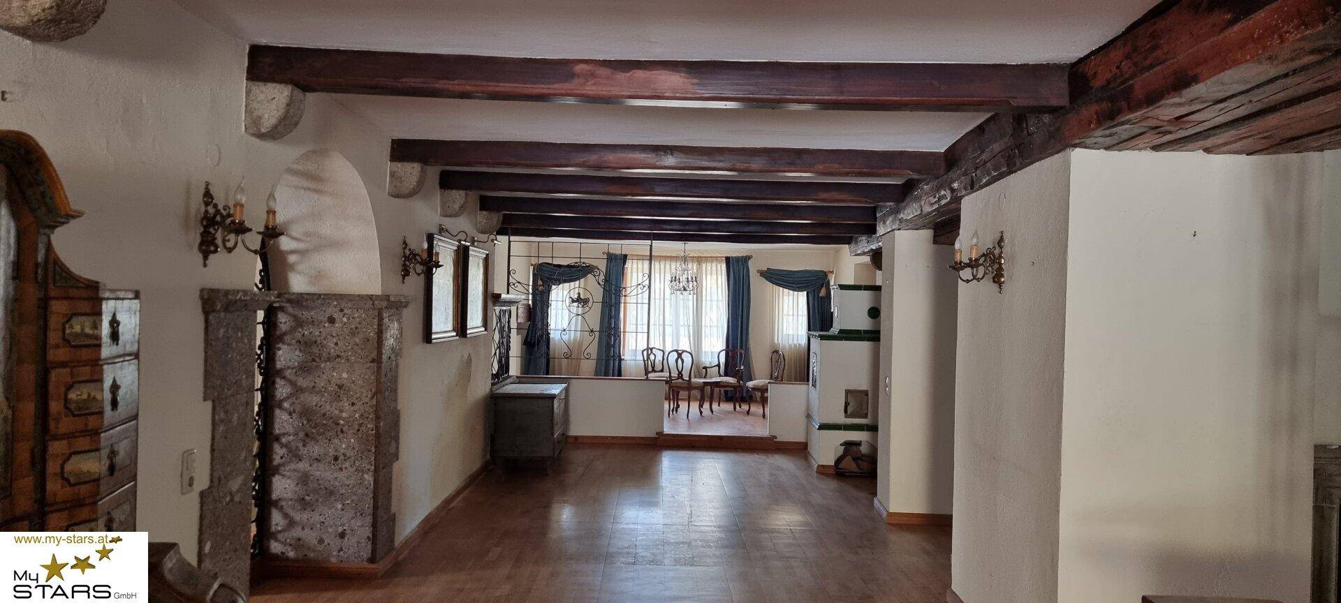 Rustikales Wohnzimmer mit Holzbalkendecke, Kachelofen und Holzboden.