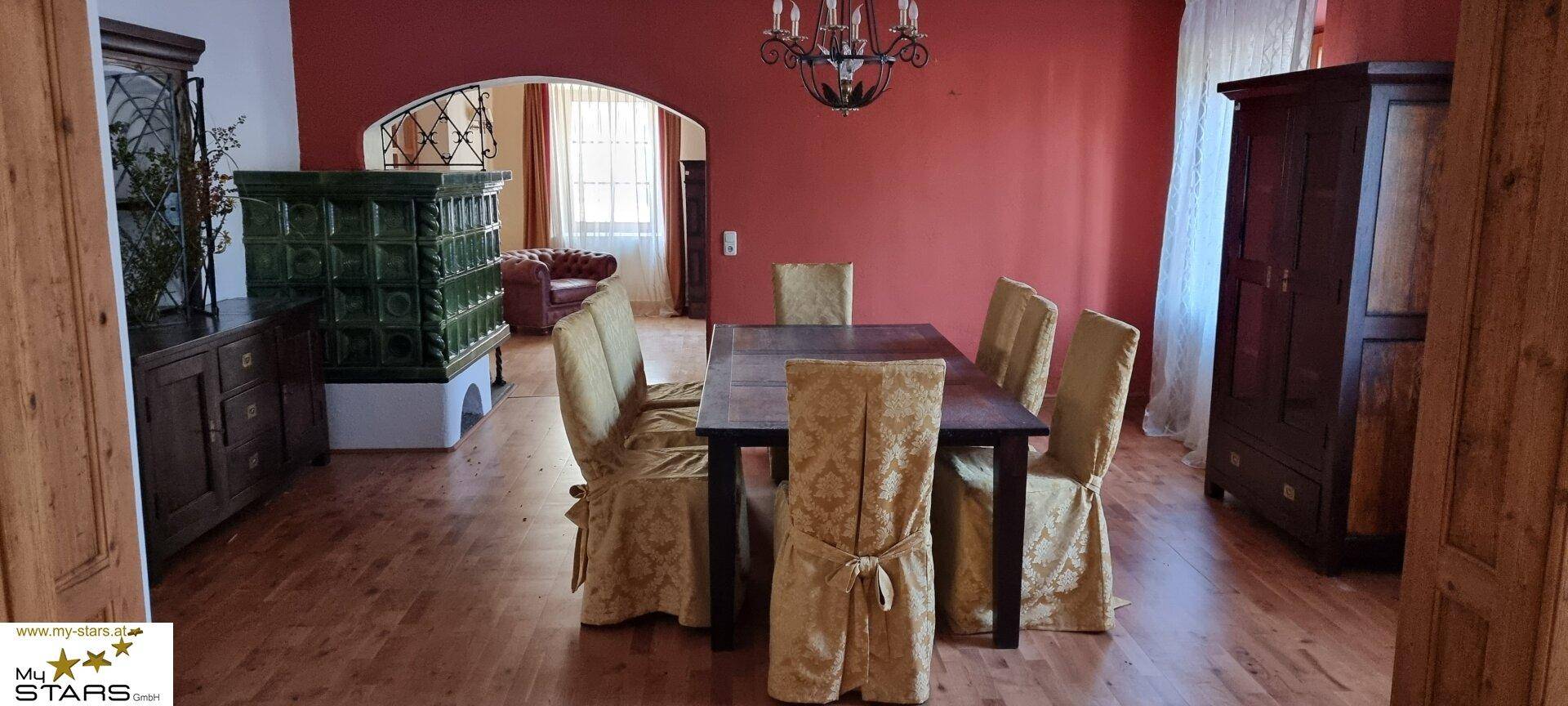 Elegantes Esszimmer mit großem Holztisch, Kachelofen und traditionellen Möbeln.
