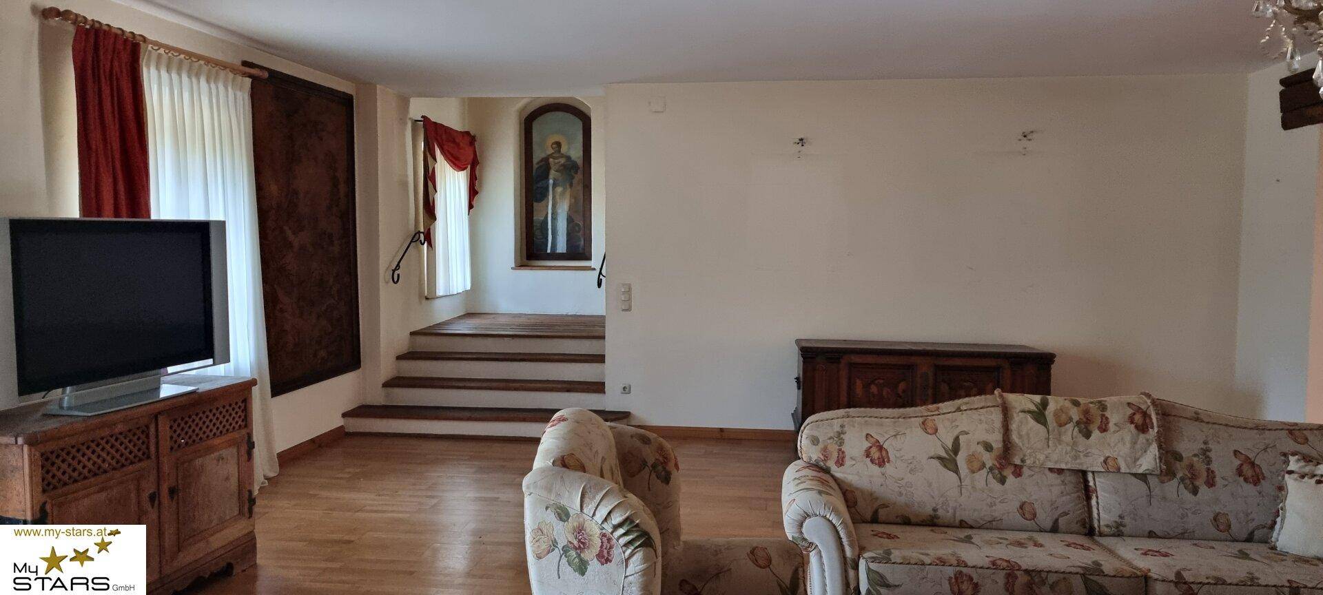 Helles Wohnzimmer mit Fernseher, Parkettboden und Treppenaufgang zu weiteren Räumen.