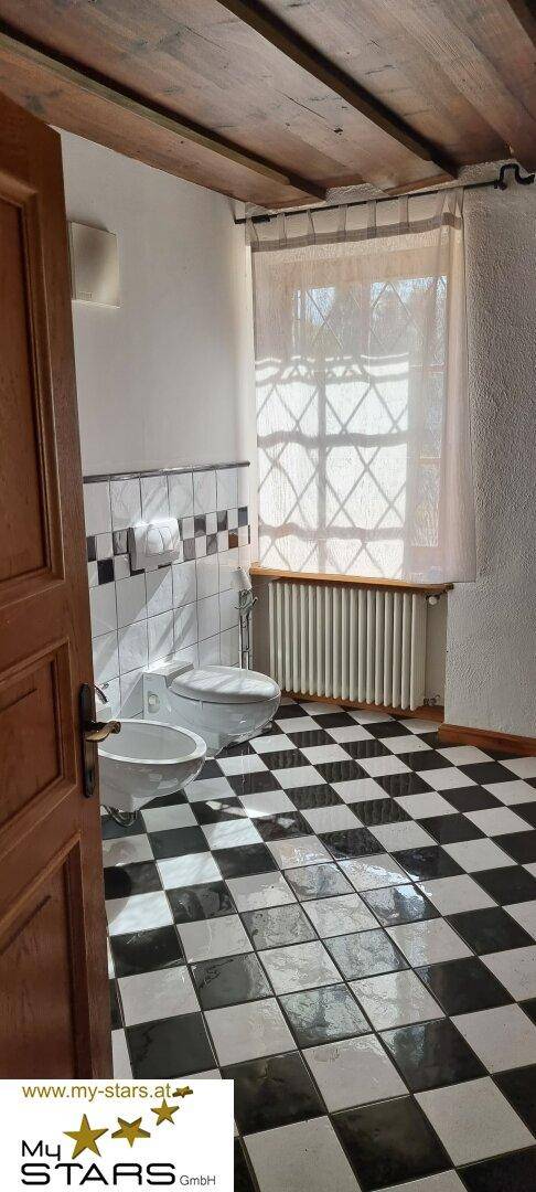 Badezimmer mit schwarz-weiß karierten Fliesen, WC, Bidet und Fenster.