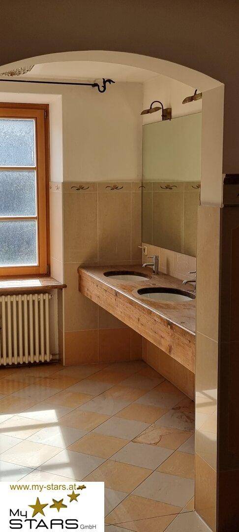 Badezimmer mit Doppelwaschbecken aus Holz und Fliesenboden, hell durch ein Fenster.