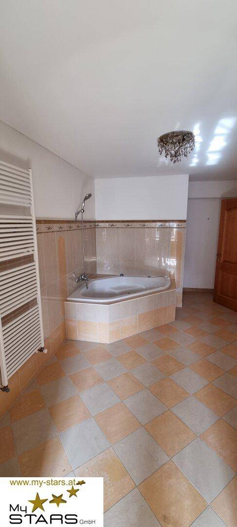 Geräumiges Badezimmer mit Eckbadewanne, Handtuchheizkörper und gemustertem Fliesenboden.