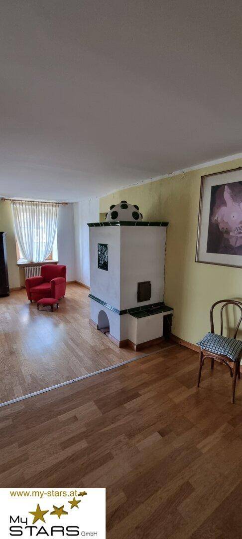 Gemütliches Wohnzimmer mit traditionellem Kachelofen, Holzboden und Fenster.