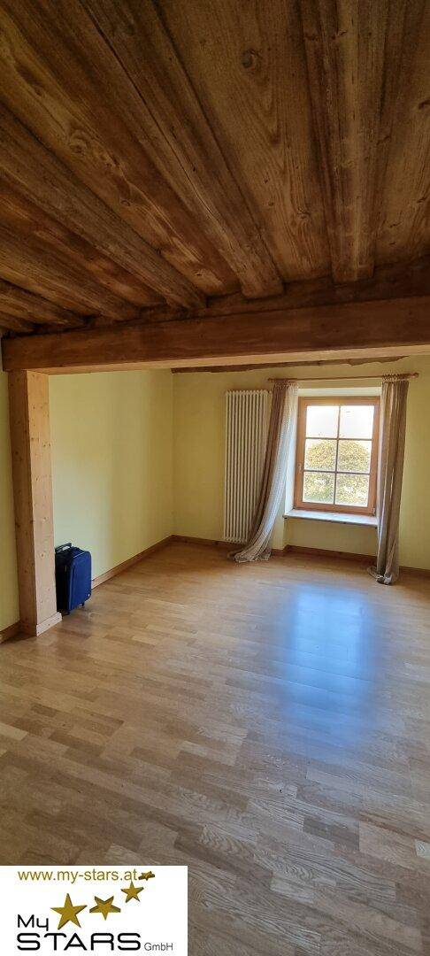 Helles Zimmer mit Holzbalken, Parkettboden und einem Fenster, das viel Licht spendet.