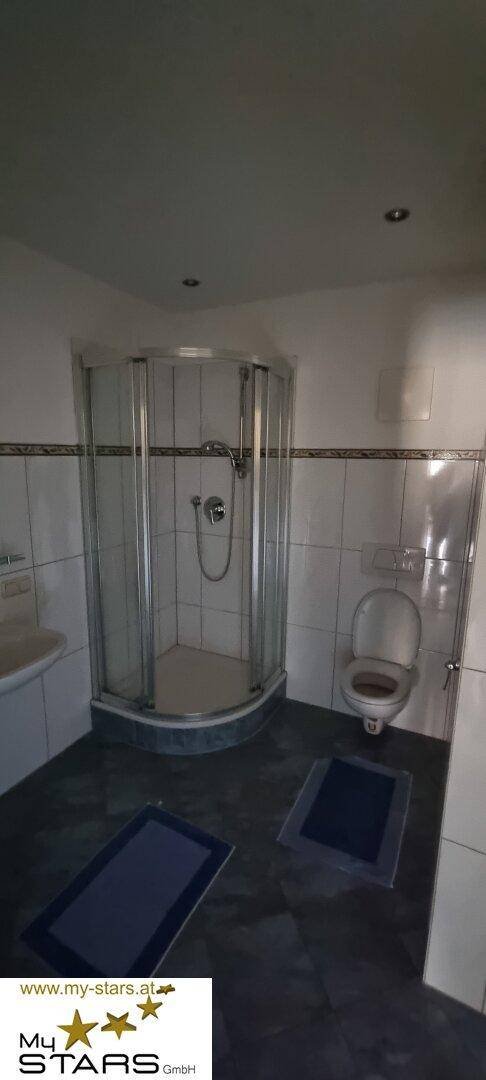 Badezimmer mit Duschkabine, WC und dunklem Fliesenboden, funktional eingerichtet.