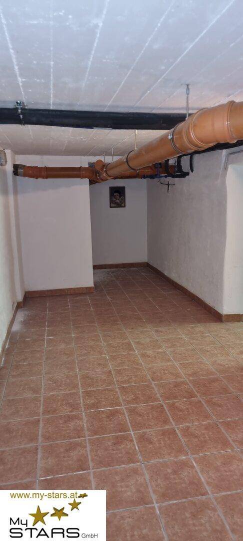 Geräumiger Kellerraum mit sichtbaren Rohren an der Decke und gefliestem Boden.