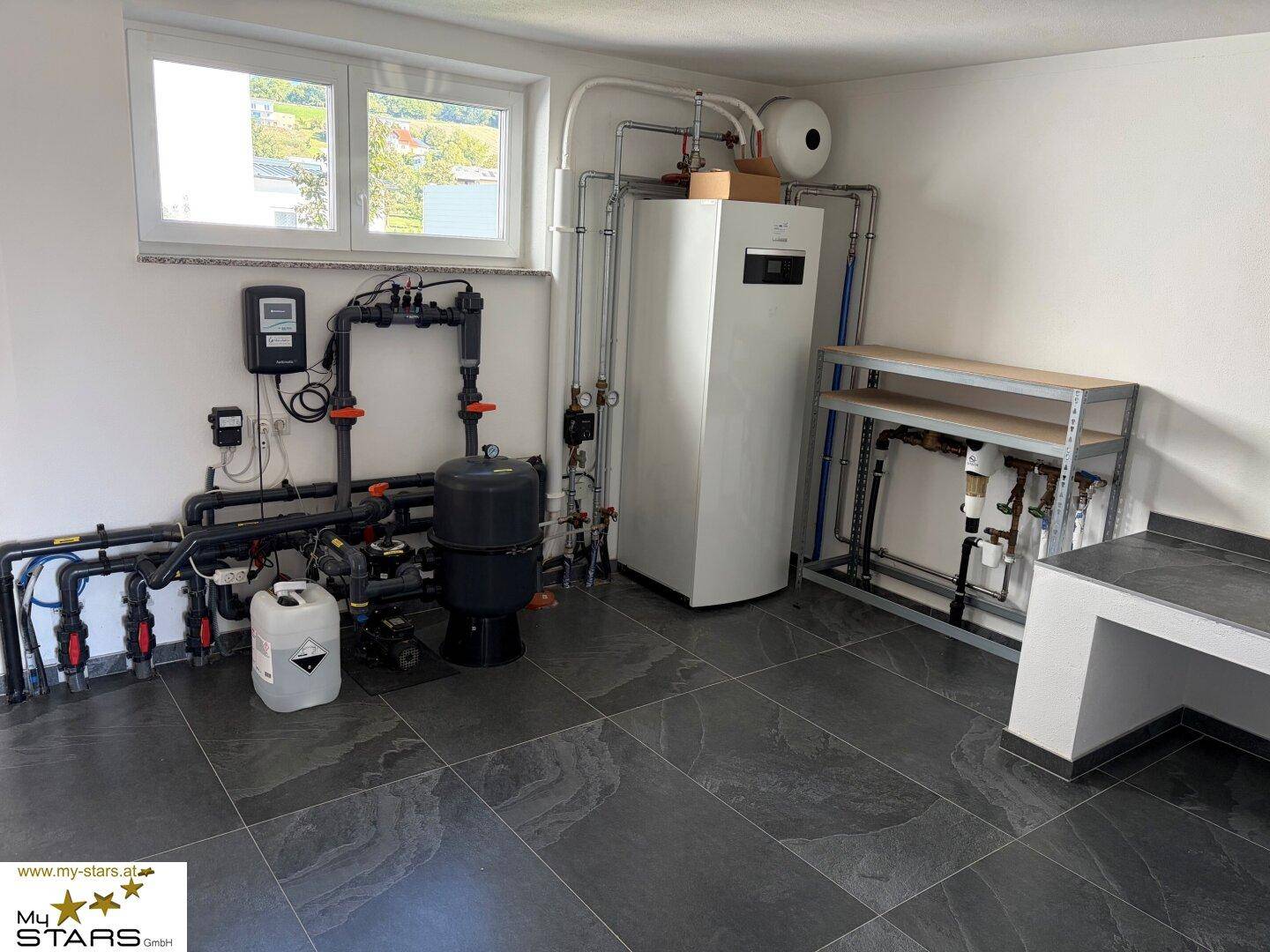 Technikraum mit Wärmepumpe, Wasserinstallationen und Regalen für Lagerung.