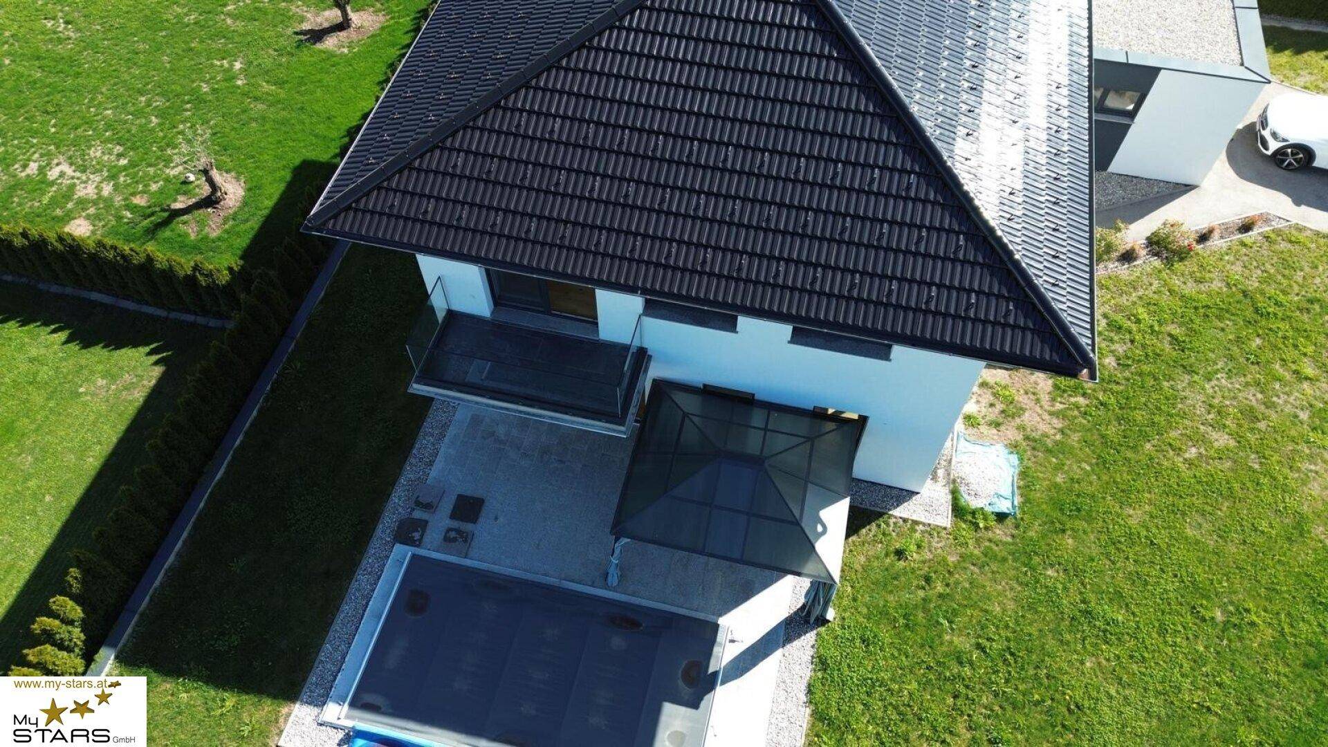 Dachansicht eines modernen Hauses mit schwarzem Ziegeldach und Gartenbereich mit Pool.