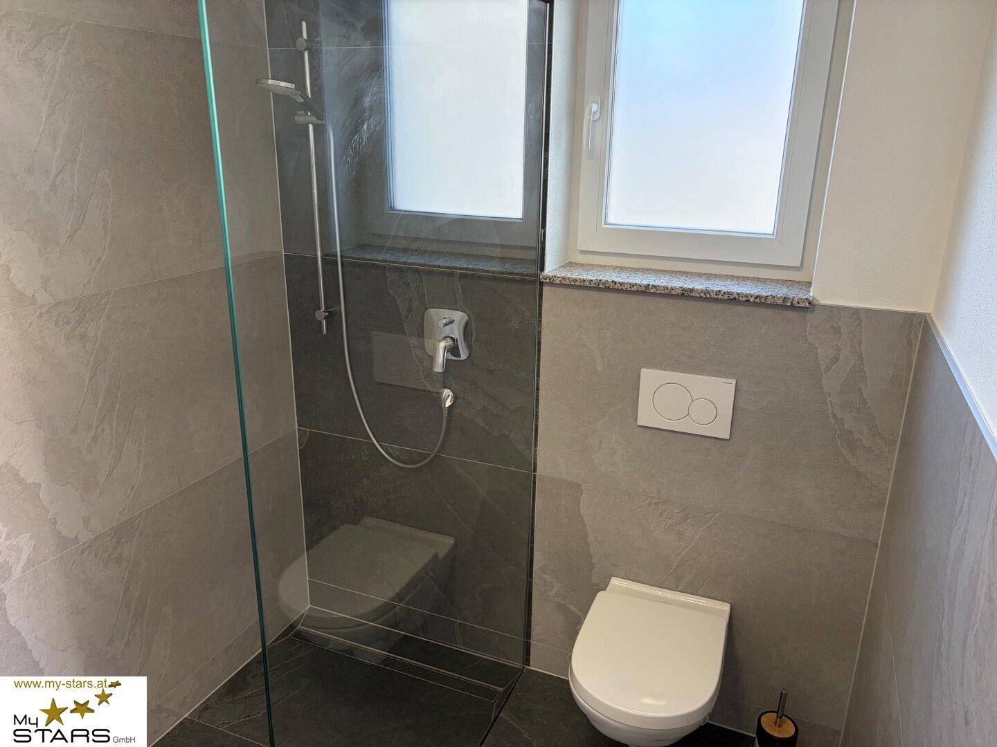 Modernes Badezimmer mit ebenerdiger Dusche, Toilette und grauen großformatigen Fliesen.