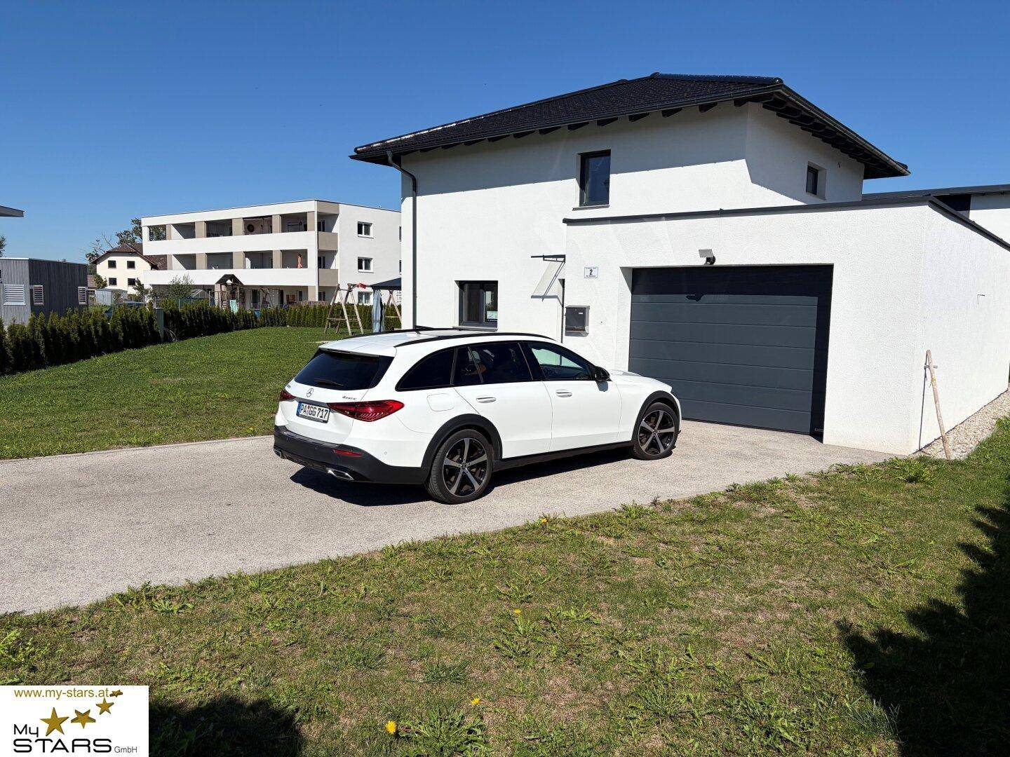 Modernes Einfamilienhaus mit Garage und gepflegtem Vorgarten an einem sonnigen Tag.