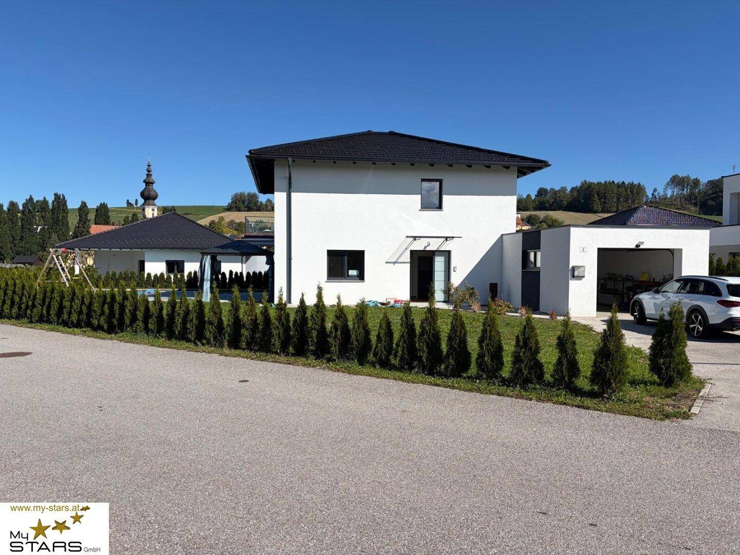 Modernes Einfamilienhaus mit Garage, Garten und Hecke unter blauem Himmel.