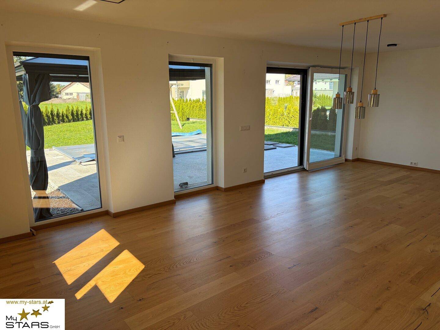 Helles Wohnzimmer mit Holzboden und großen Fenstern, die Zugang zum Garten bieten.