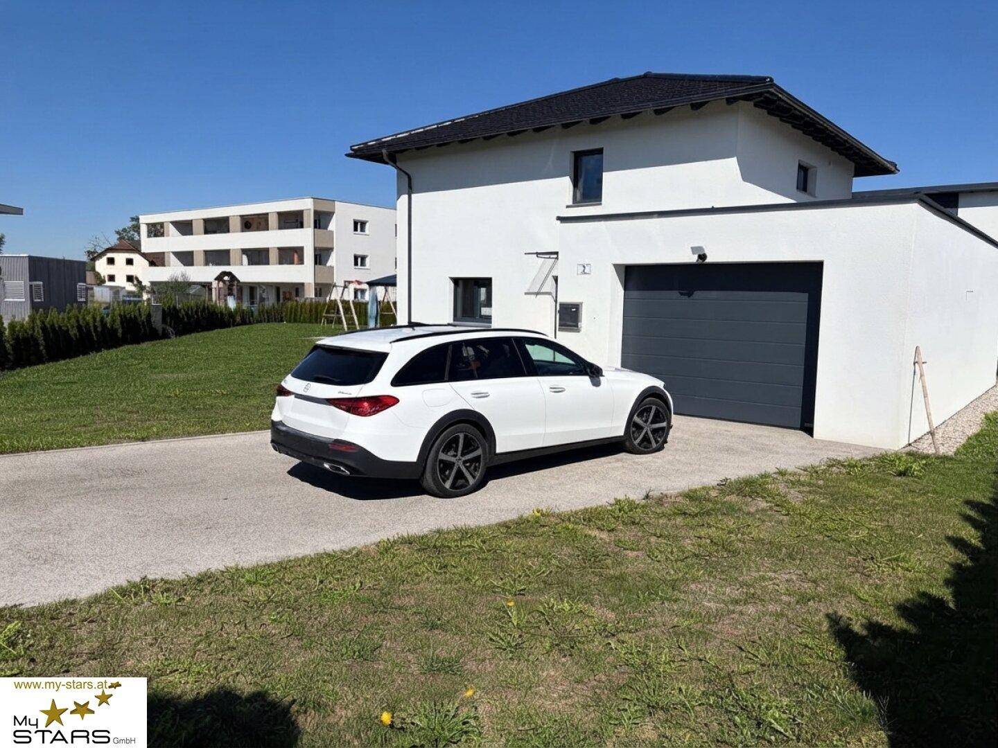 Modernes Einfamilienhaus mit weißer Fassade, integrierter Garage und gepflegtem Vorgarten an einem sonnigen Tag.